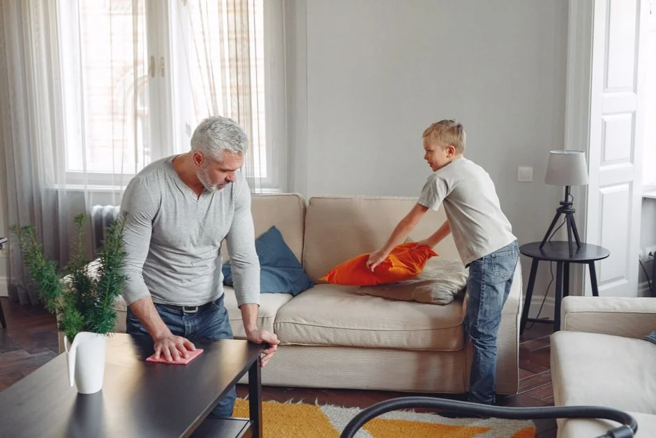 Two women in work clothes cleaning a modern living room using a vacuum and mop.